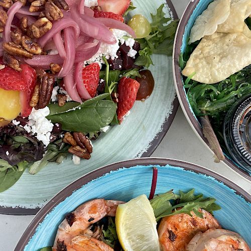 The image shows three bowls of food: a salad with strawberries and nuts, a green salad with chips, and a shrimp dish with lemon and sauce.