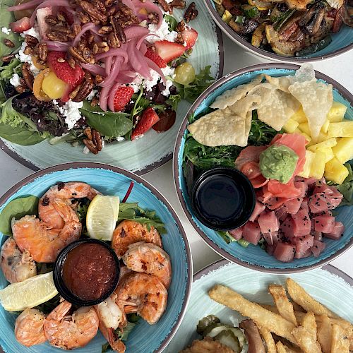 This image shows several plates of food, including a salad, grilled shrimp, a meat dish with chips, and a burger with fries.