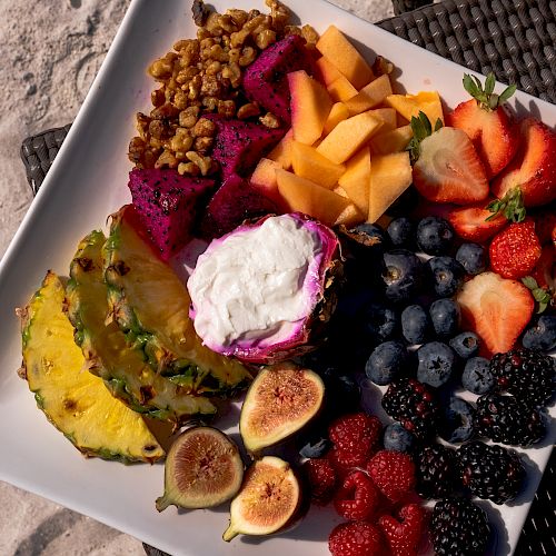 A platter of assorted fruits, including pineapple, dragon fruit, melon, strawberries, blueberries, blackberries, raspberries, figs, granola, and yogurt.