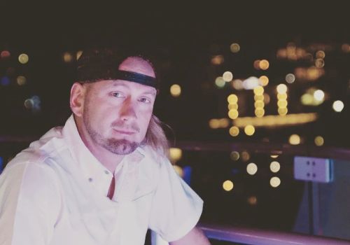 A person with a headband and white shirt is seated outdoors at night, with blurred city lights in the background.