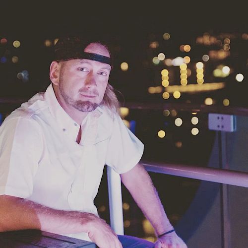 A person with a headband and white shirt is seated outdoors at night, with blurred city lights in the background.