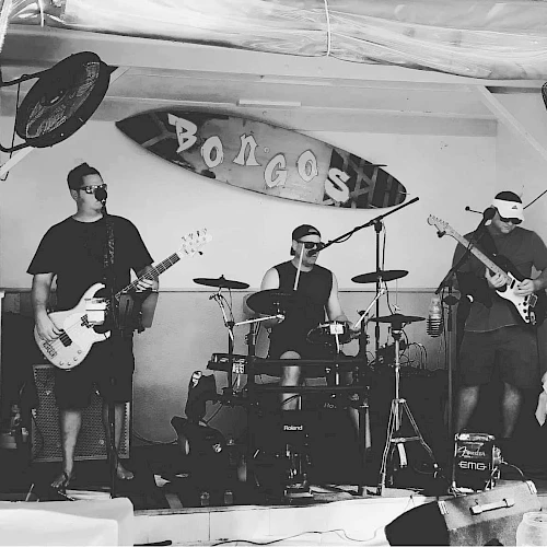 The image shows a black-and-white photo of a band performing at a venue called "Bongos," with members playing guitar, bass, and drums.
