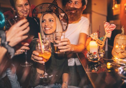 A group of people in Halloween costumes are celebrating and raising their drinks together. There are festive decorations on the table.