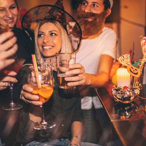 A group of people in Halloween costumes are celebrating and raising their drinks together. There are festive decorations on the table.