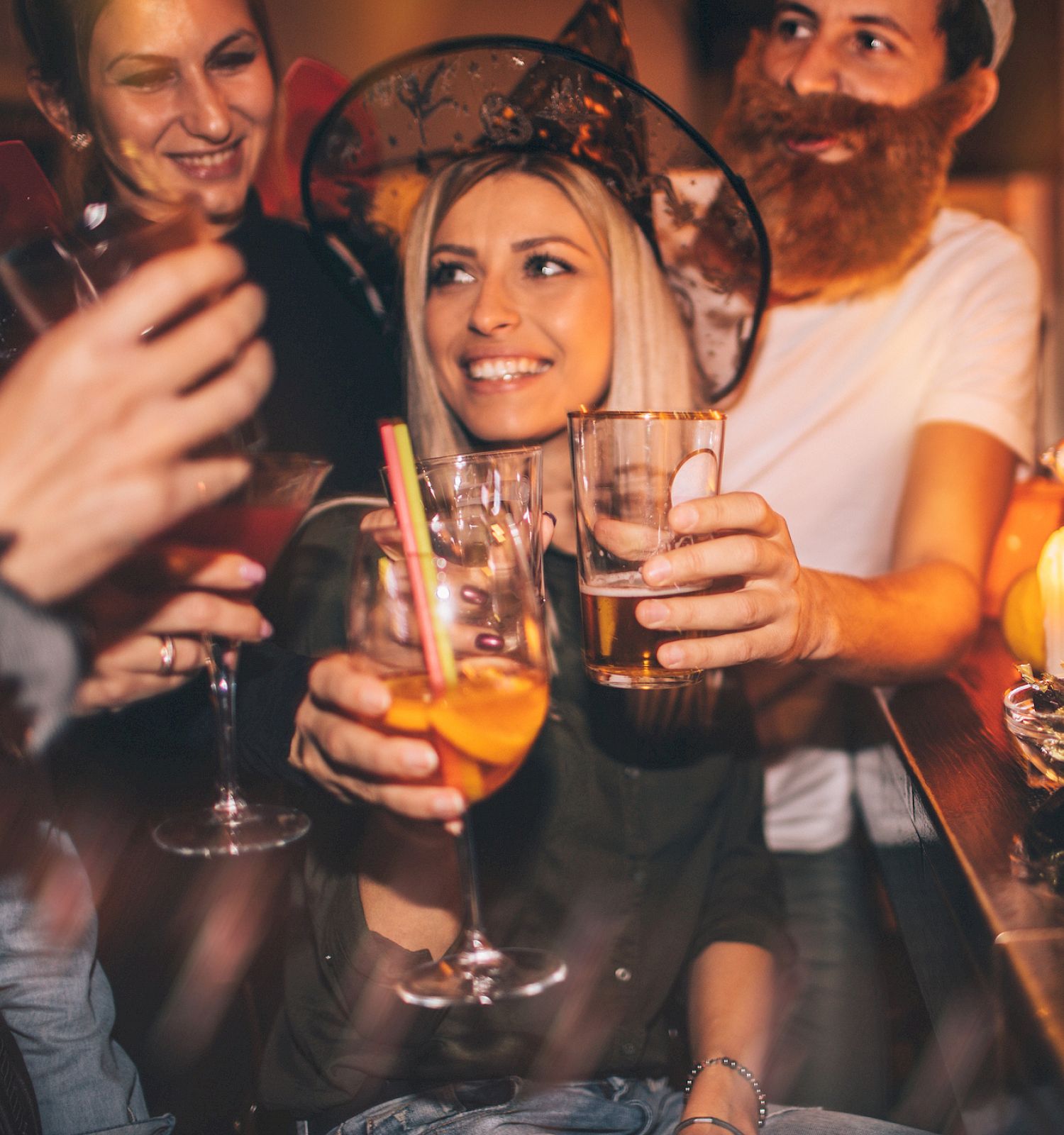 A group of people in costumes enjoying drinks at a festive party, with Halloween decorations like candles, candy, and pumpkins on the table.