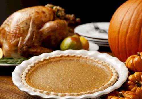 A Thanksgiving meal setup featuring a roast turkey, a pumpkin pie, pumpkins, and fruits, with plates and utensils on the table.