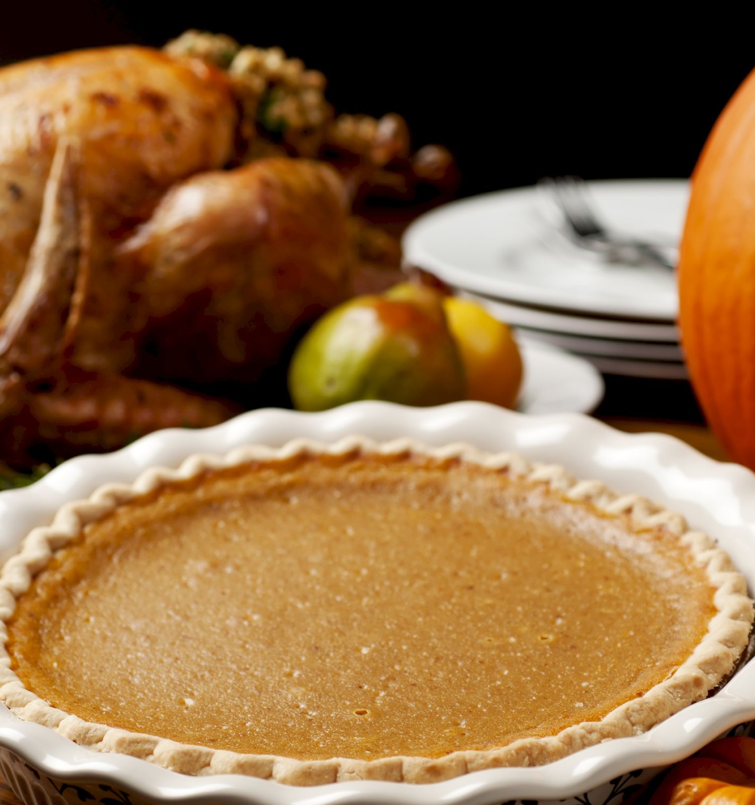 This image displays a Thanksgiving meal setup with a turkey, pumpkin pie, pumpkins, and fruits on a wooden table.