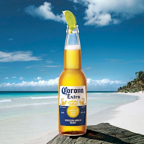 A bottle of Corona Extra beer with a lime wedge in the neck, set against a tropical beach background with clear blue skies and sandy shores.