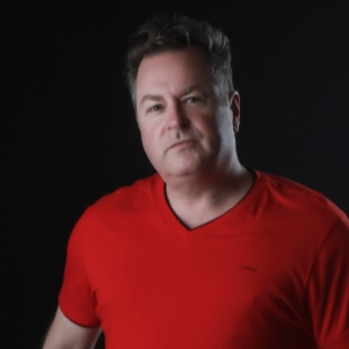 A person wearing a red shirt is posing in front of a dark background.